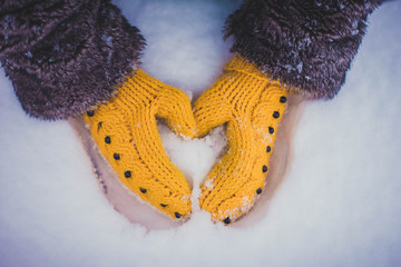 hands in mittens make a heart out of snow