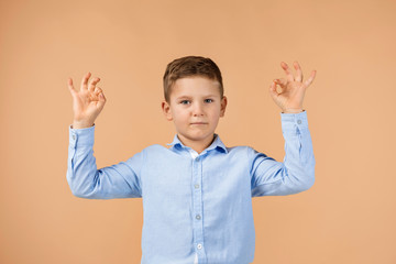 Wall Mural - cute little boy in shirt making Ok gesture on beige background.