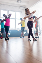 Low Angle View Of Attractive Zumba Trainer Exercising With Multicultural Dancers In Studio