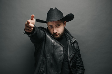 Wall Mural - Cowboy studio portrait of a man wearing learher jacket and a hat with serious face