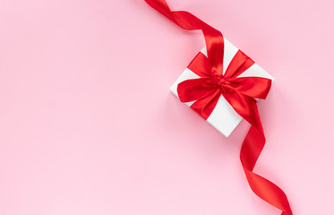 White gift box with  red ribbon on pink background. Top view. Holiday time at any time of the year