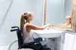 Blonde girl in wheelchair turning on the water in a bathroom