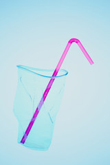 Squashed plastic cup and drink straw over blue background. Collecting plastic waste to recycling. Concept of plastic pollution and too many plastic waste. Copy space at the top