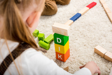 cropped view of children playing with wooden blocks with kid word on carpet