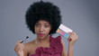 © Fractal Pictures - Portrait of pretty playful afro-american woman with make-up beauty tools in hands. Beauty afro model girl holding and demonstrating eye shadows palette with a brush on grey background.