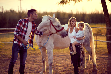 Wall Mural - Mom and dad showing the horse to a little girl . Fun on countryside, sunset golden hour. Freedom nature concept.