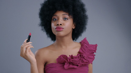 Portrait of funny cheerful african girl in coquettish mood opening pink lipstick posing in a studio against grey background.