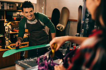 Wall Mural - selective focus of smiling worker cleaning ski with brush and colleague on background