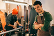 © LIGHTFIELD STUDIOS - selective focus of smiling worker with crossed arms and his colleague using wax iron in repair shop