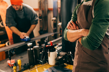 Wall Mural - cropped view of worker with crossed arms and his colleague using wax iron in repair shop