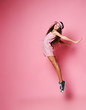 Slim teenager girl in a cap and pink striped dress is jumping back arched with her arms outstretched on a pink