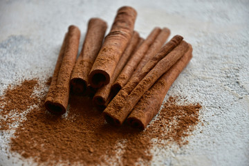 Cinnamon sticks and cinnamon powder on a stone background. Close-up. Side view. Natural light.