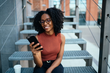glad african american lady communicating with friend on phone in street