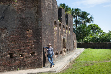 Old fortress brick wall of Fort Zeelandia on a clear Sunny day and a standing man in a cowboy hat, Guyana. World tourism, attractions, fortress.