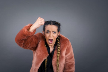 Sticker - Fierce confident European dark-haired woman holding fist in front of her as if is ready for fight or challenge, screaming and having aggressive expression on face. Isolated over gray background.