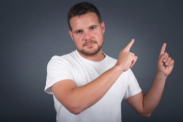 Advertisement concept. Positive, pretty, caucasion man with beaming smile in jeans shirt on grey background is pointing with his two index finger and looking on empty copy space.