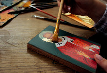 Hand With Brush Of Gold Leaf. Artist Applies Gold Leaf To The Icon. Reproduction Of The Icon Of St. Nicholas. The Process Of The Artist's Work. Brushes And Paints On The Background.