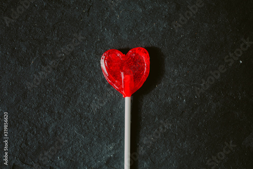 Photographie Close up view of red heart shaped lollipop on black slate background