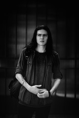 Wall Mural - a black-and-white photo of a young man with long, dark hair and brown eyes, a face with freckles, walking down the street in a stylish shirt and jeans,in a Cagle style, in a sad mood