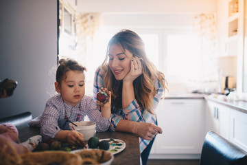 A mother and her daughter painting eggs for Easter in their kitchen.