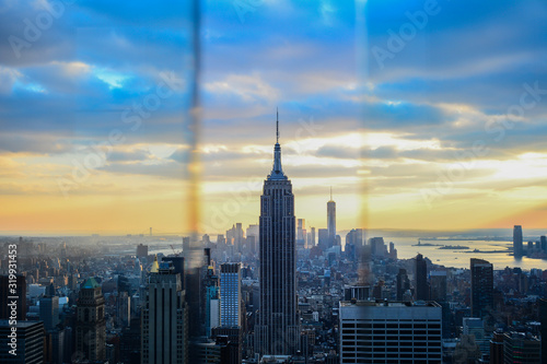 Fotomural Empire State Building in city against cloudy sky seen through window during suns