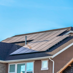square frame gray roof of home with solar panels and pipe vents against blue sky background