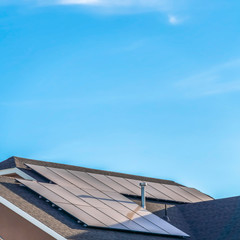 square gray roof of home with solar panels and pipe vents against blue sky background