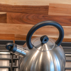 Wall Mural - Square frame Kettle on the cooktop against wooden chopping board and tile backsplash