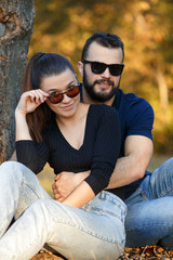 Portrait of a man and a woman in sunglasses in the woods. Young stylish couple on the background of nature. Warm autumn evening in the forest.