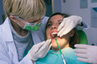 © qunica.com - Female dentist in dental office examines the mouth and teeth of a female patient