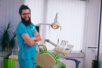 Wall Mural - Positive and smiling bearded dentist standing in his dental office