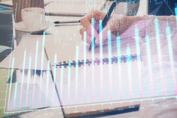 Forex chart hologram on hand taking notes background. Concept of analysis. Double exposure