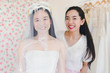 © Nawarit - The bridesmaid is helping the beautiful bride wearing a white wedding dress in front of the mirror.
