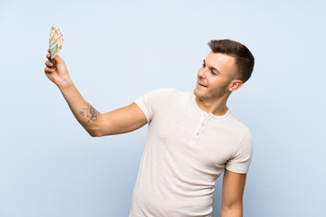 Wall Mural - Young handsome blonde man over isolated blue background taking a lot of money