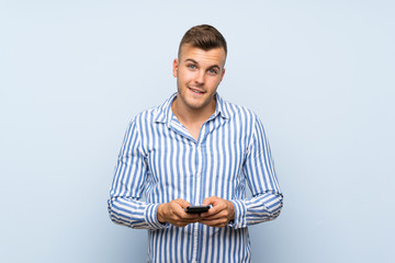 Wall Mural - Young handsome blonde man over isolated blue background sending a message with the mobile