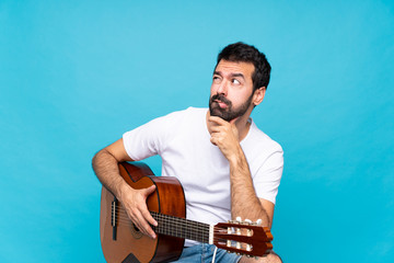 Wall Mural - Young man with guitar over isolated blue background with confuse face expression