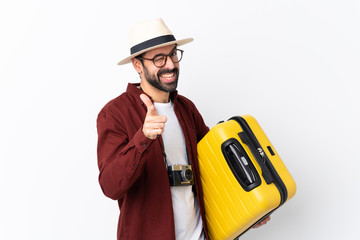 Traveler man man with beard holding a suitcase over isolated white background pointing to the front and smiling