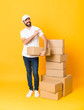 © luismolinero - Full-length shot of delivery man among boxes over isolated yellow background pointing to the side to present a product