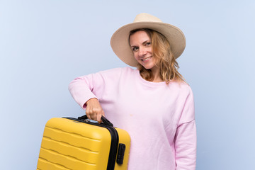 Blonde woman over isolated background in vacation with travel suitcase and a hat