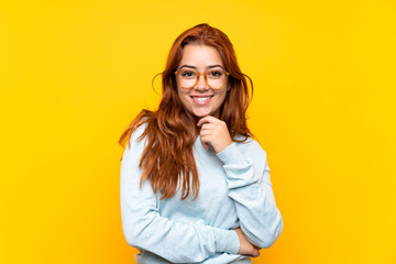 Wall Mural - teenager redhead girl over isolated yellow background with glasses and smiling