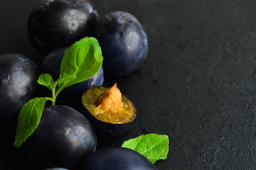 Wall Mural - Closeup view of fresh organic plums with mint leaves over black background