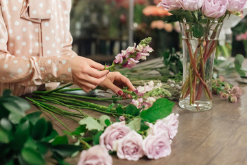 Beautiful smiling female florist in apron arranging bouquet in flower shop