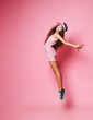 Teen girl in stylish cap and pink striped dress is jumping pointing her toes with her arms outstretched on a pink