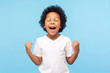 © khosrork - Child winning, success. Portrait of excited little boy in T-shirt raising hands and screaming delighted with victory and luck, expressing extreme joy. indoor studio shot isolated on blue background