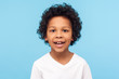 Closeup portrait of amazing cheerful little boy with curly hairdo in white T-shirt looking at camera with happy carefree smile and missed milk teeth. indoor studio shot isolated on blue background