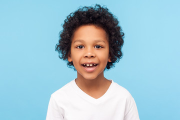 closeup portrait of amazing cheerful little boy with curly hairdo in white t-shirt looking at camera