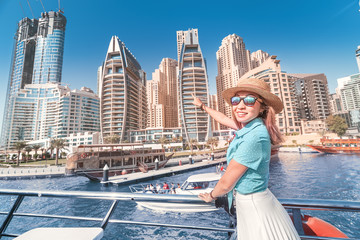 Wall Mural - Cheerful girl traveler on a ferry boat sailing through Dubai Marina port among huge skyscrapers. Concept of tourism in the UAE