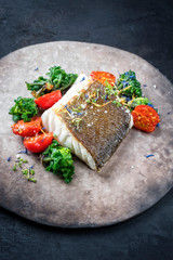 Wall Mural - Gourmet fried European skrei cod fish filet with kalette and tomatoes as closeup on a modern design plate