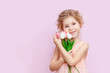 © marinatynik - Cute little blonde girl with curly hair holding a bouquet of tulips. Studio portrait. Girl with tulips. Mother's day, March 8, international women's day.