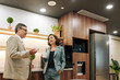 © DragonImages - Confident man and beautiful woman wearing elegant suits chatting during coffee break standing in office kitchen room